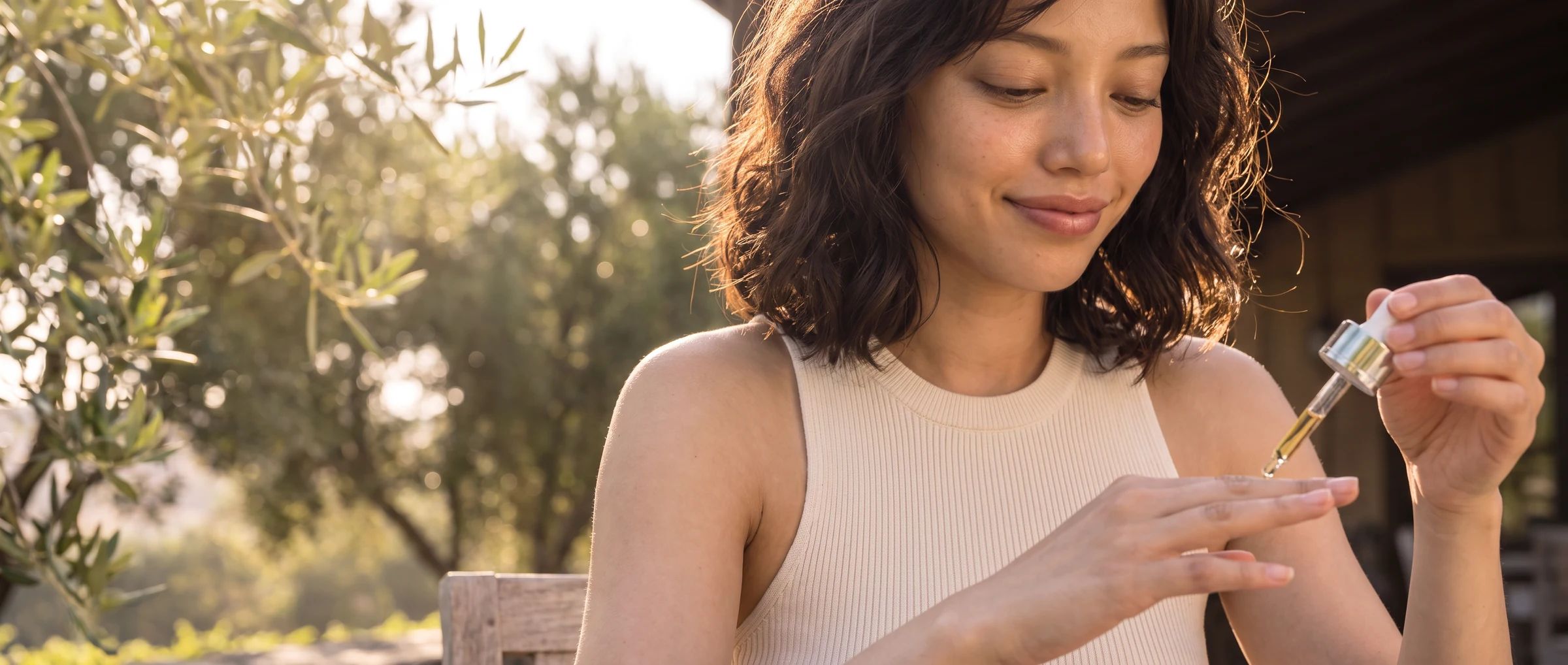 Model in a sleeveless knit top applying Glow Drop to her nails on a sunny terrace